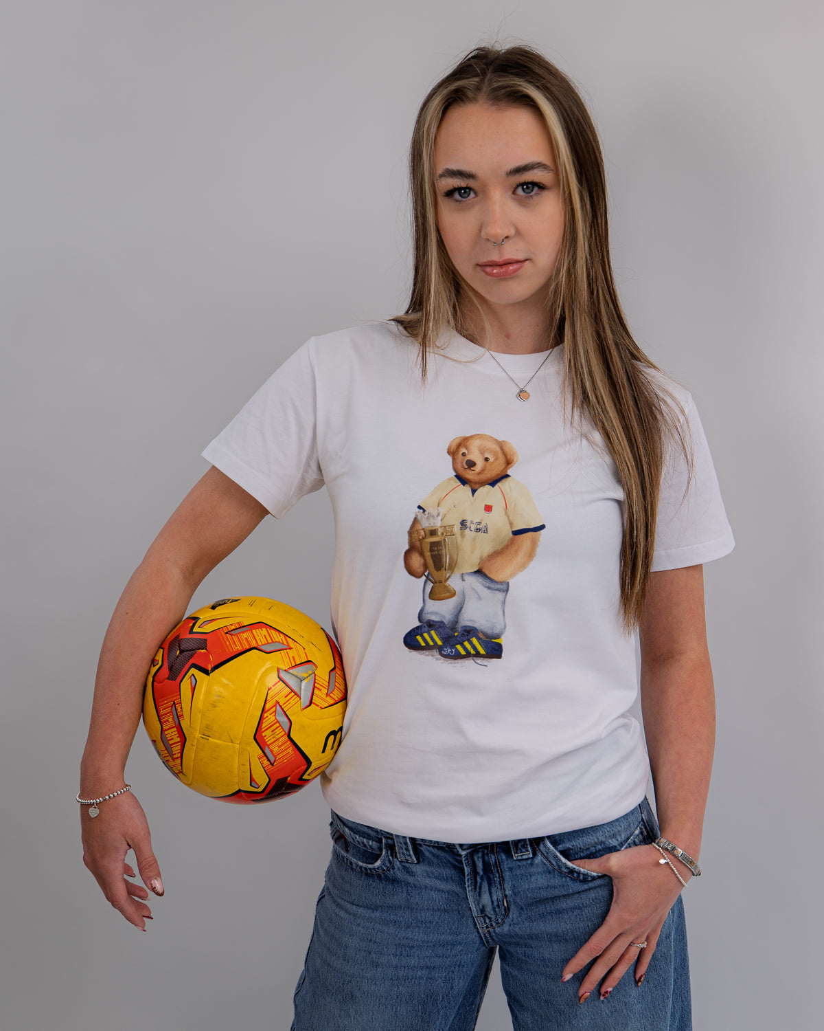 Woman wearing a white t-shirt with a bear graphic holding a soccer ball on a gray background