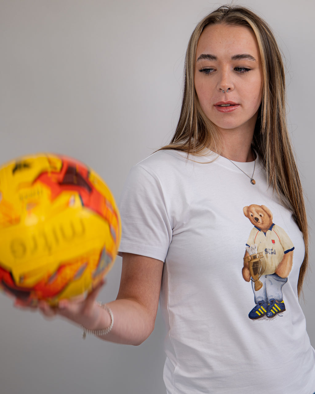 Woman wearing a white t-shirt with a bear graphic, holding a colorful ball against a plain background