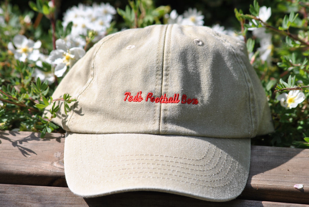 Beige cap with red text on a wooden surface with flowers in the background