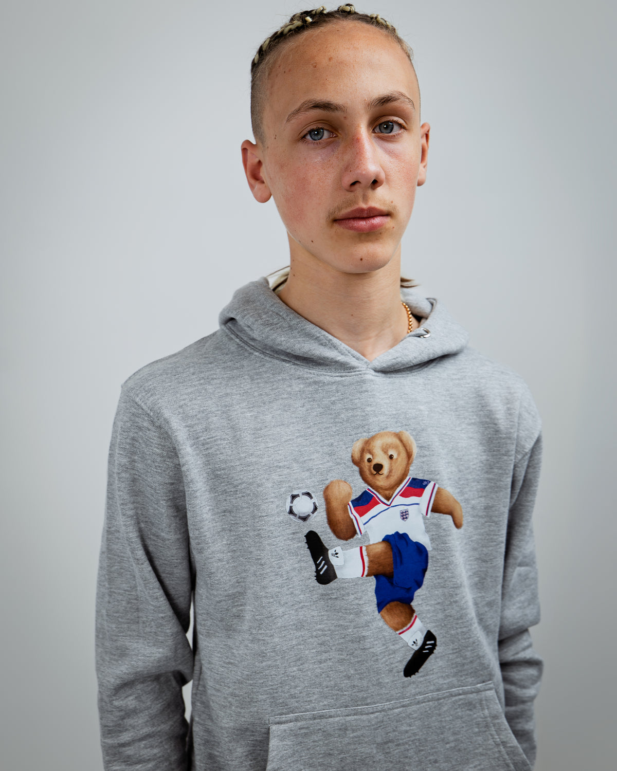 Person wearing a gray hoodie with a bear graphic holding a soccer ball on a plain background