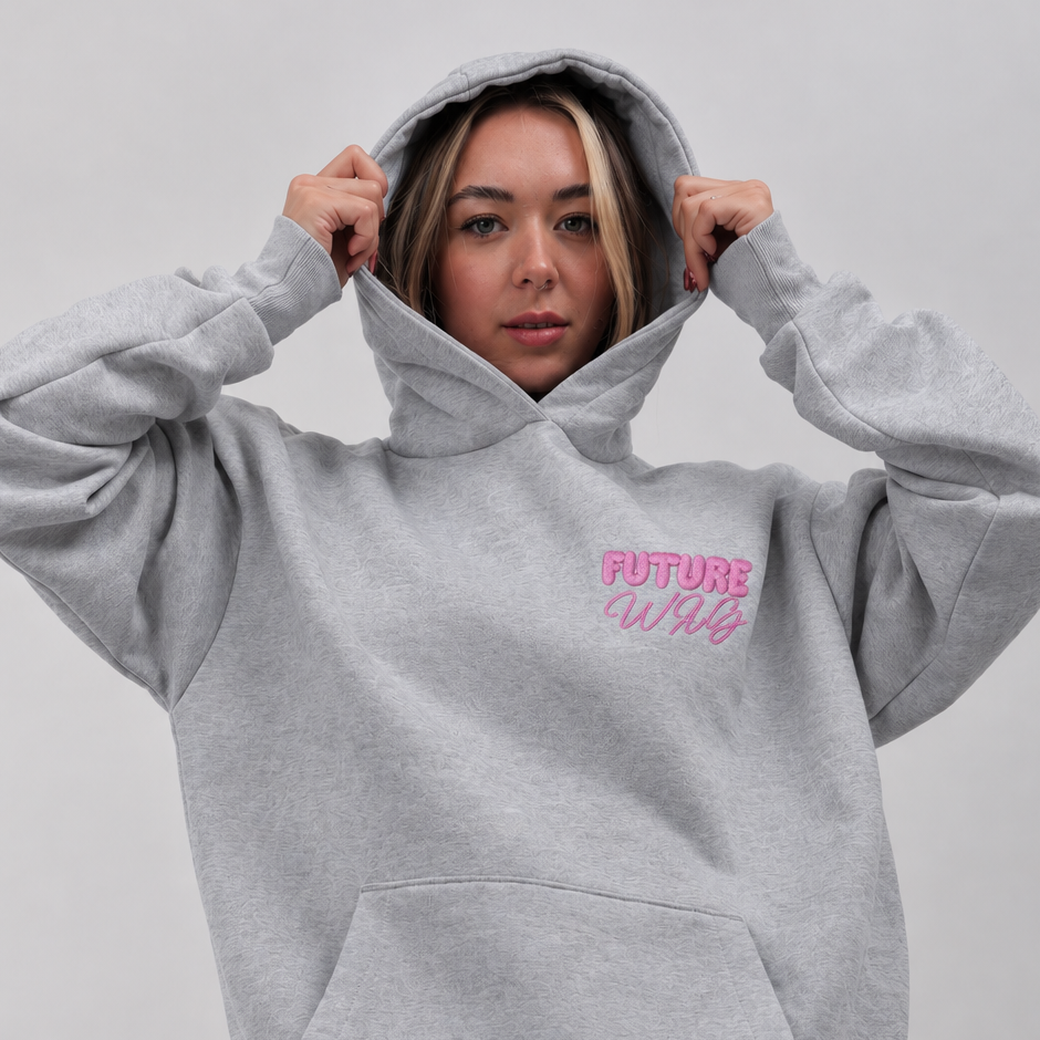 A woman wearing a light gray oversized hoodie with a pink 'FUTURE WAG' graphic on the chest, paired with blue jeans, against a plain light gray background.