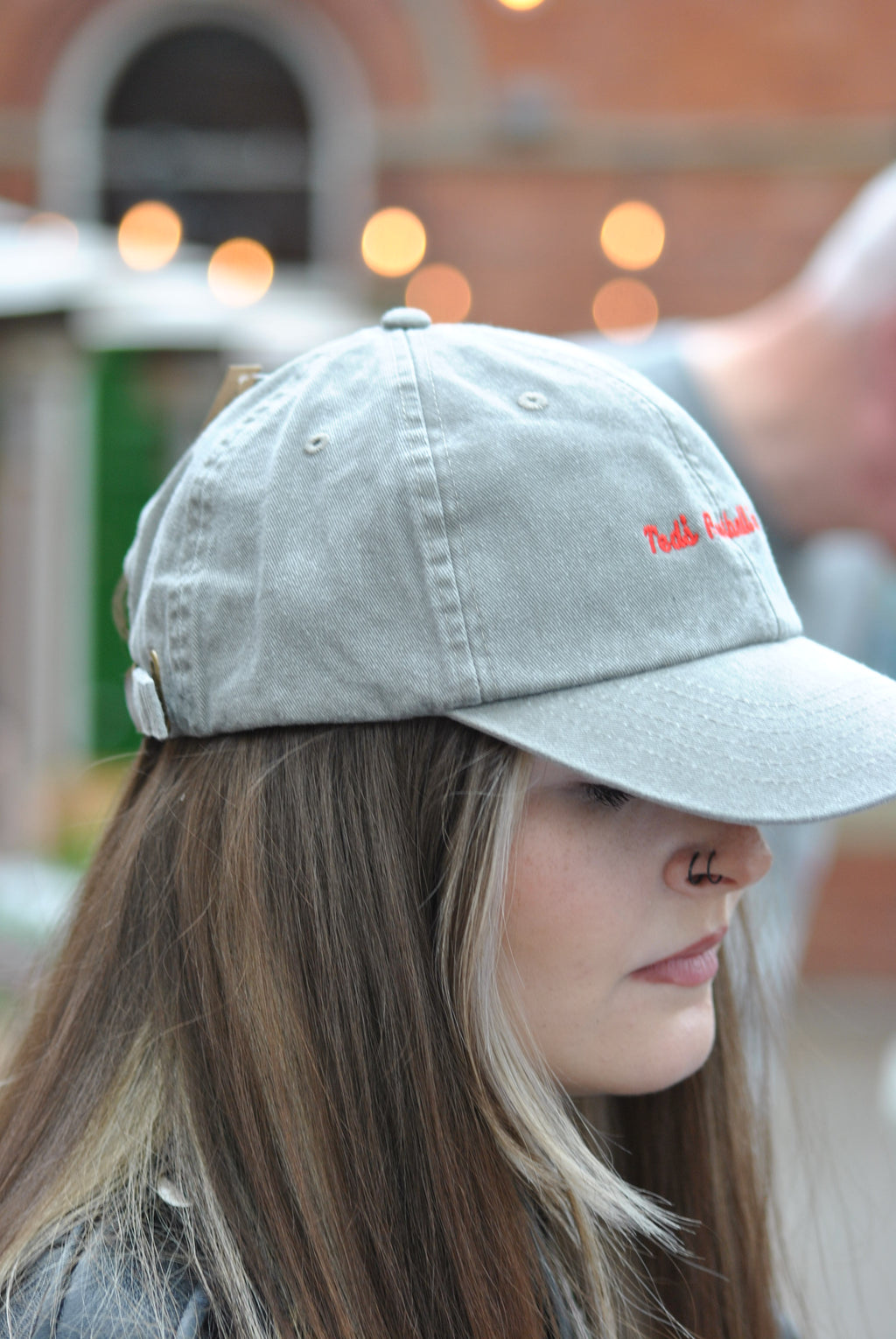 Person wearing a light gray cap red embroidered text 'teds football box'with a blurred background