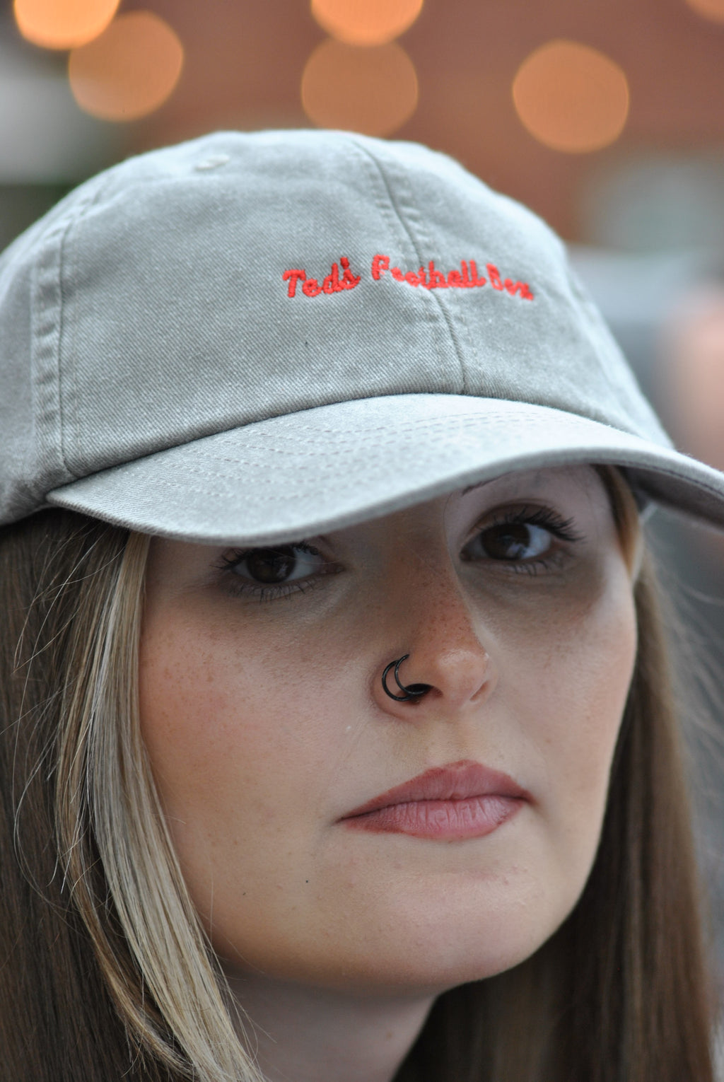 woman wearing a grey cap with 'teds football box' red embroidered text against a blurred background