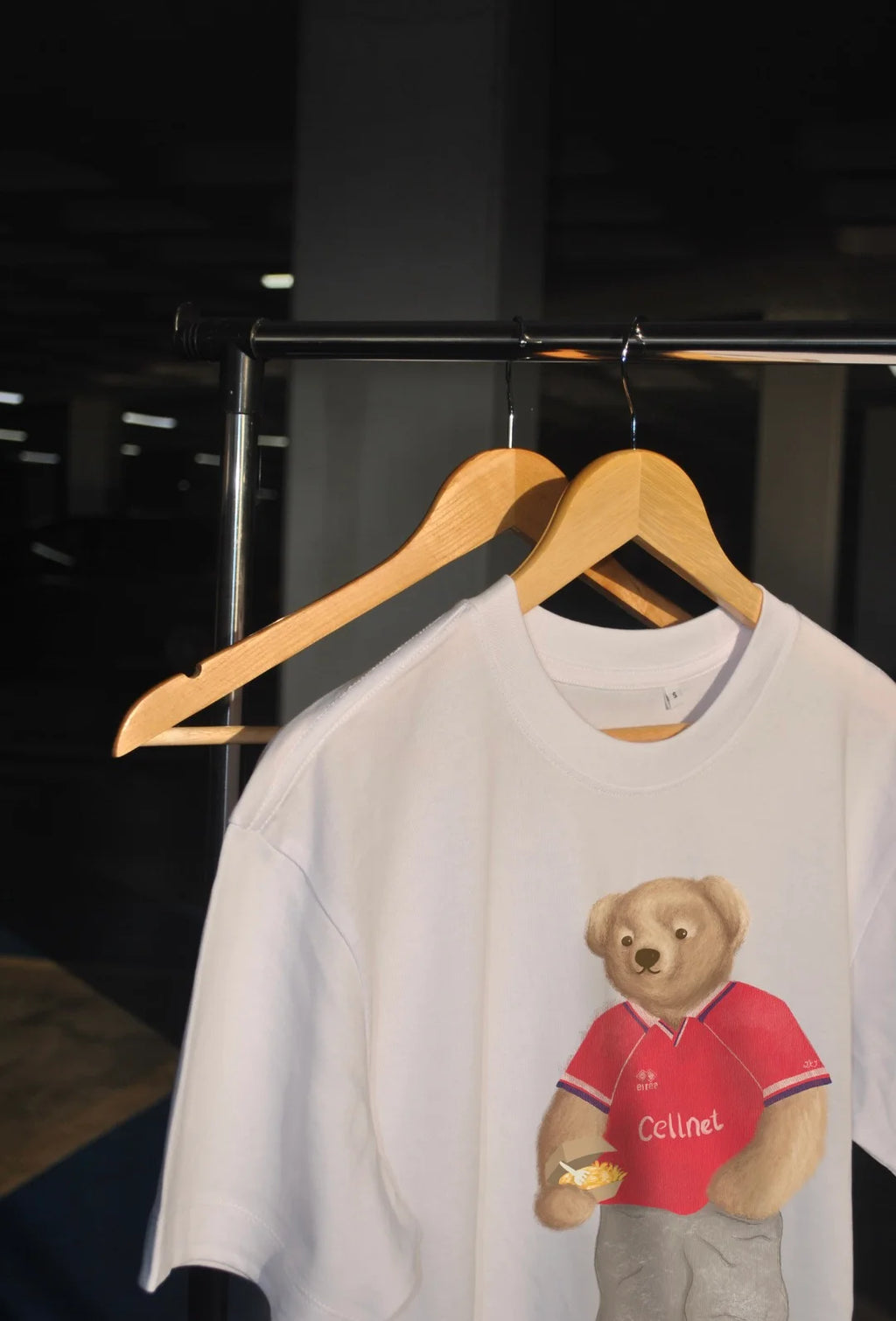 White sweatshirt with a bear graphic on a hanger against a dark background