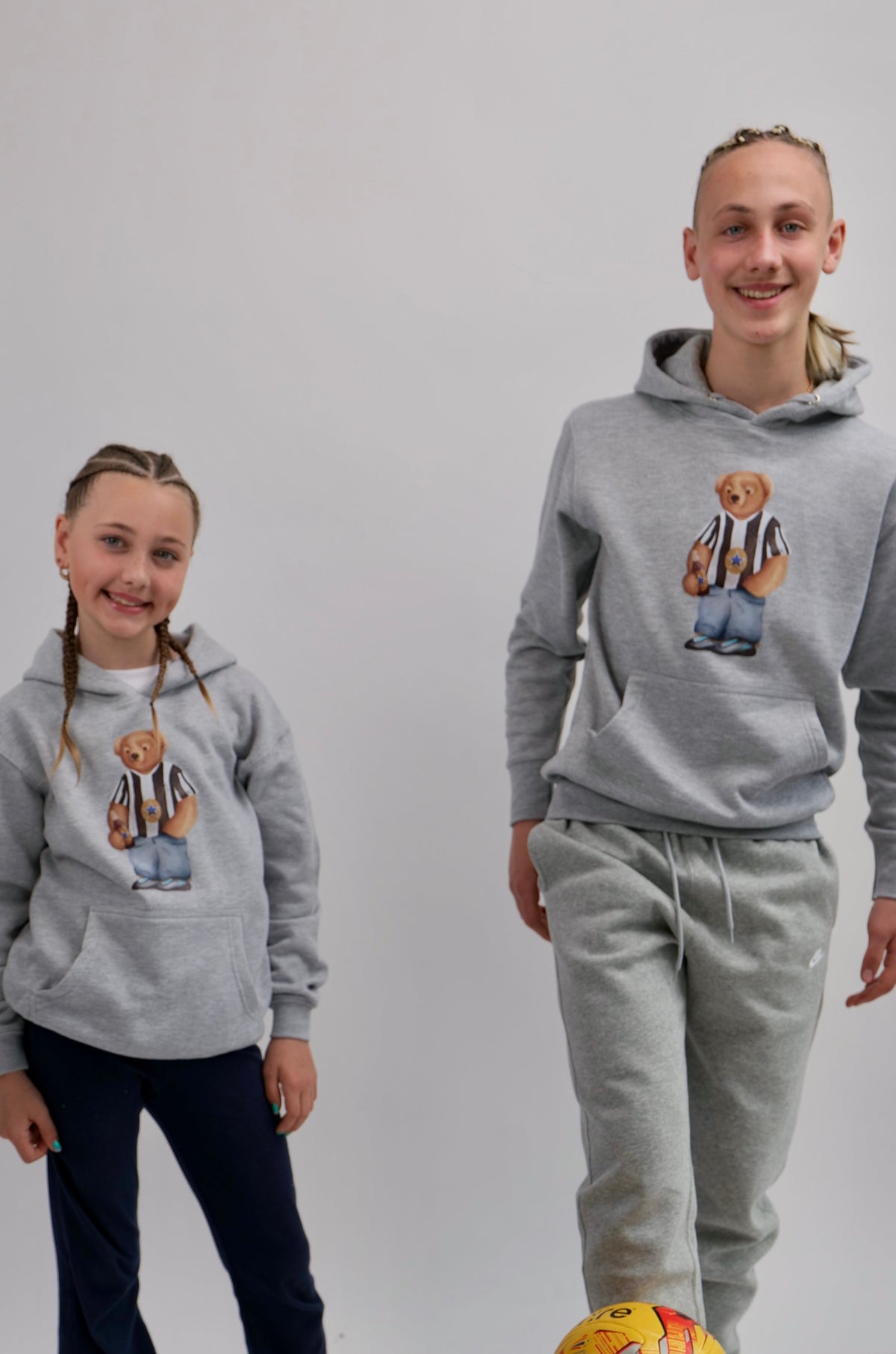 Two people wearing matching gray hoodies with a bear design on a white background.