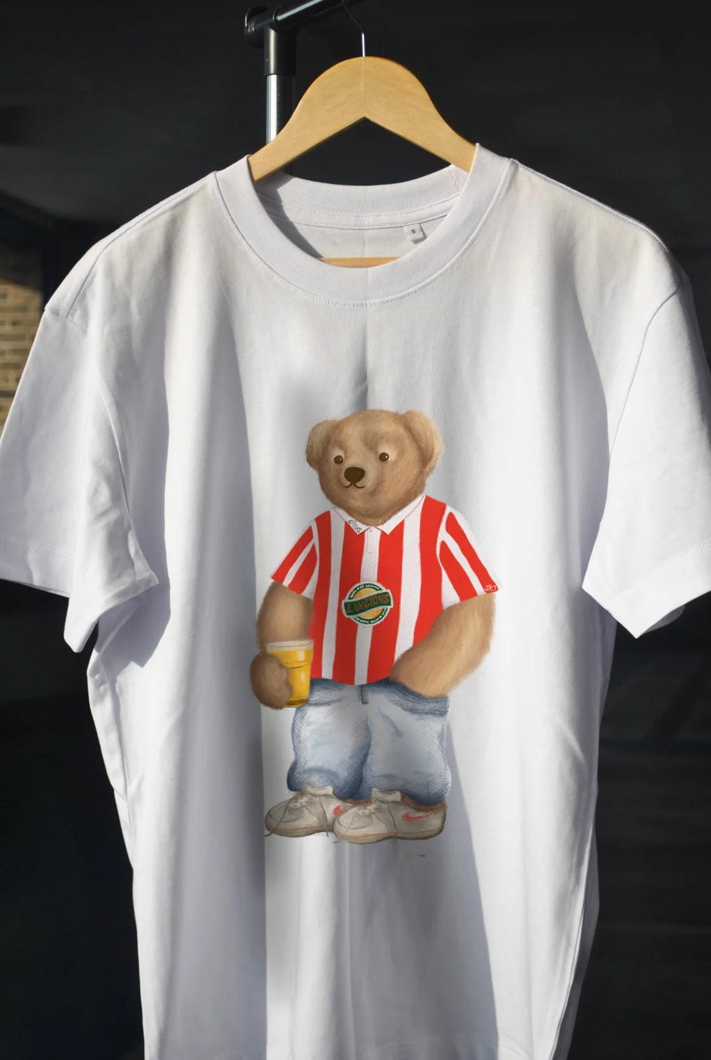 White t-shirt with a teddy bear graphic on a hanger against a black background