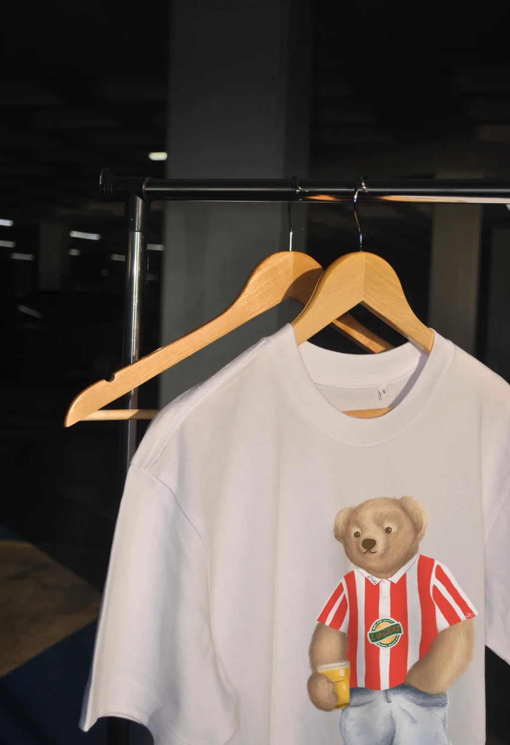 White t-shirt with a bear graphic on a hanger against a dark background
