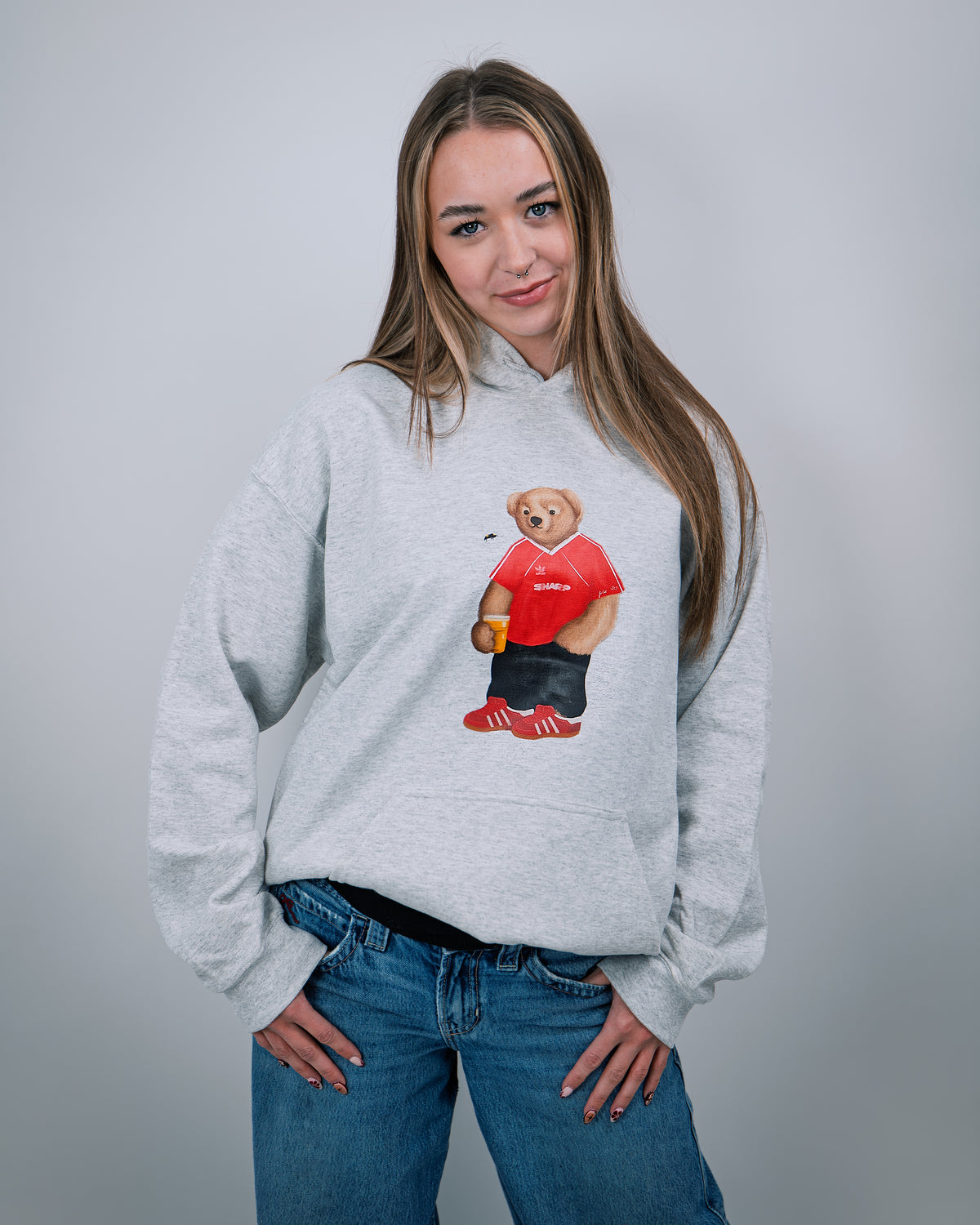Person wearing a gray hoodie with a bear graphic holding a red object on a plain background