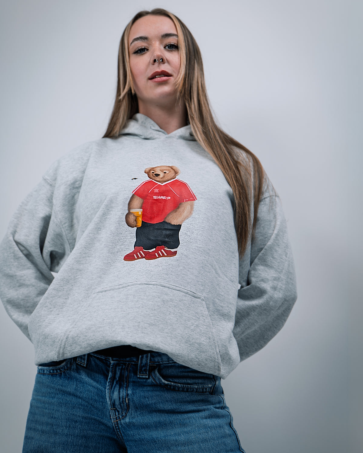 Person wearing a gray hoodie with a bear graphic holding a beer, on a plain background