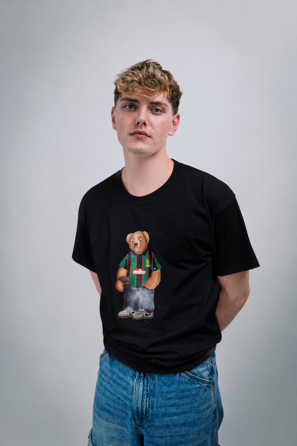 Person wearing a black t-shirt with a graphic of a aston villa bear in a sweater on a plain background
