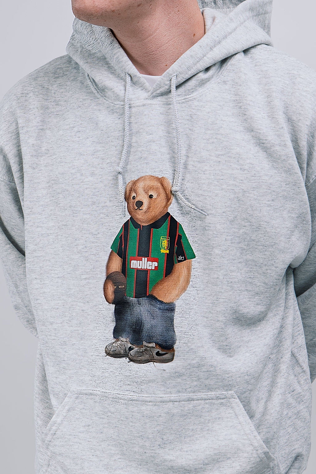 Gray hoodie with a bear graphic wearing a asyon villa shirt and jeans on a plain background