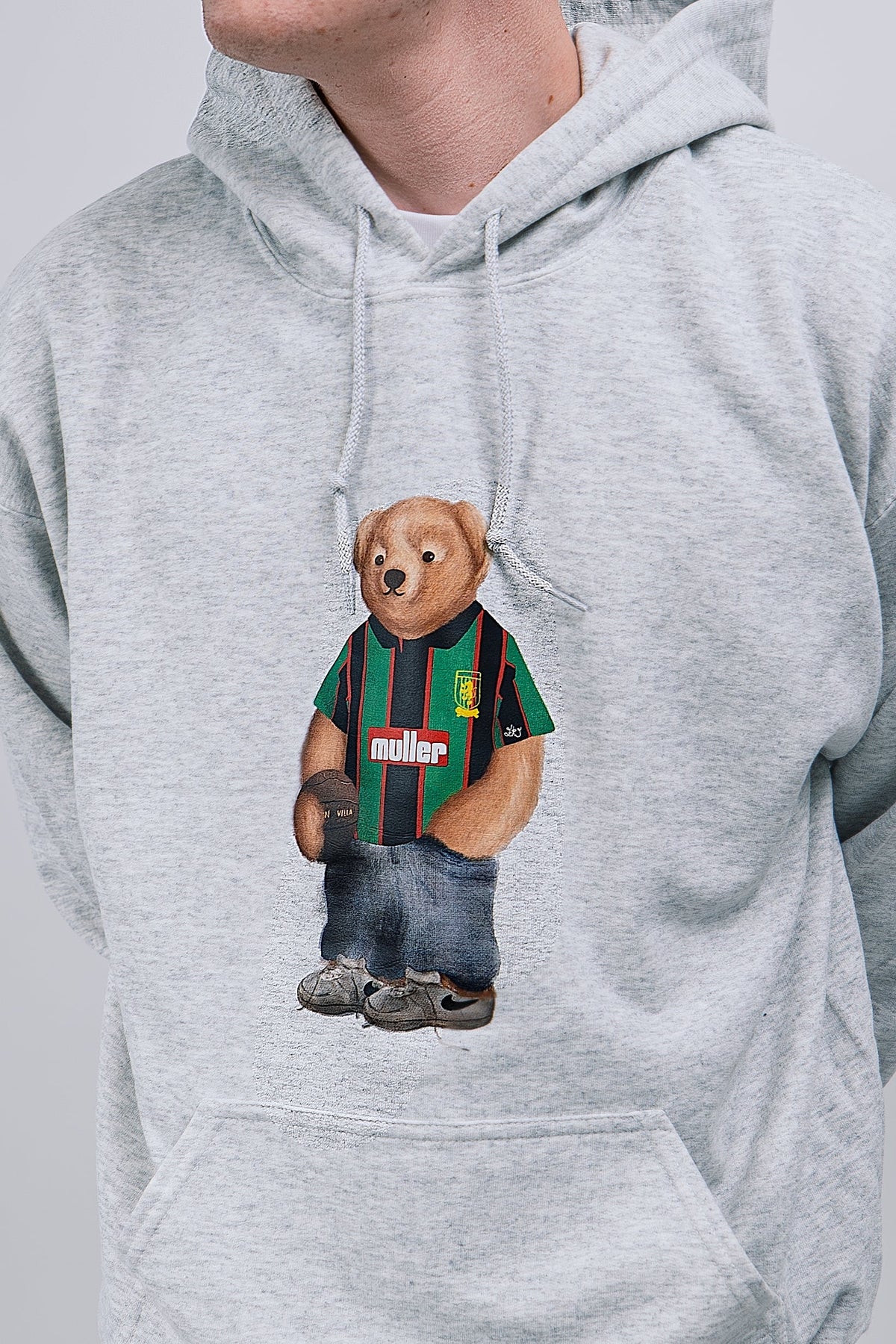 Gray hoodie with a bear graphic wearing a asyon villa shirt and jeans on a plain background
