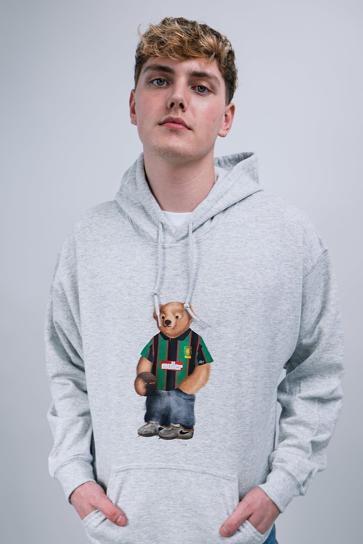 Person wearing a gray hoodie with a aston villa bear graphic on a plain background