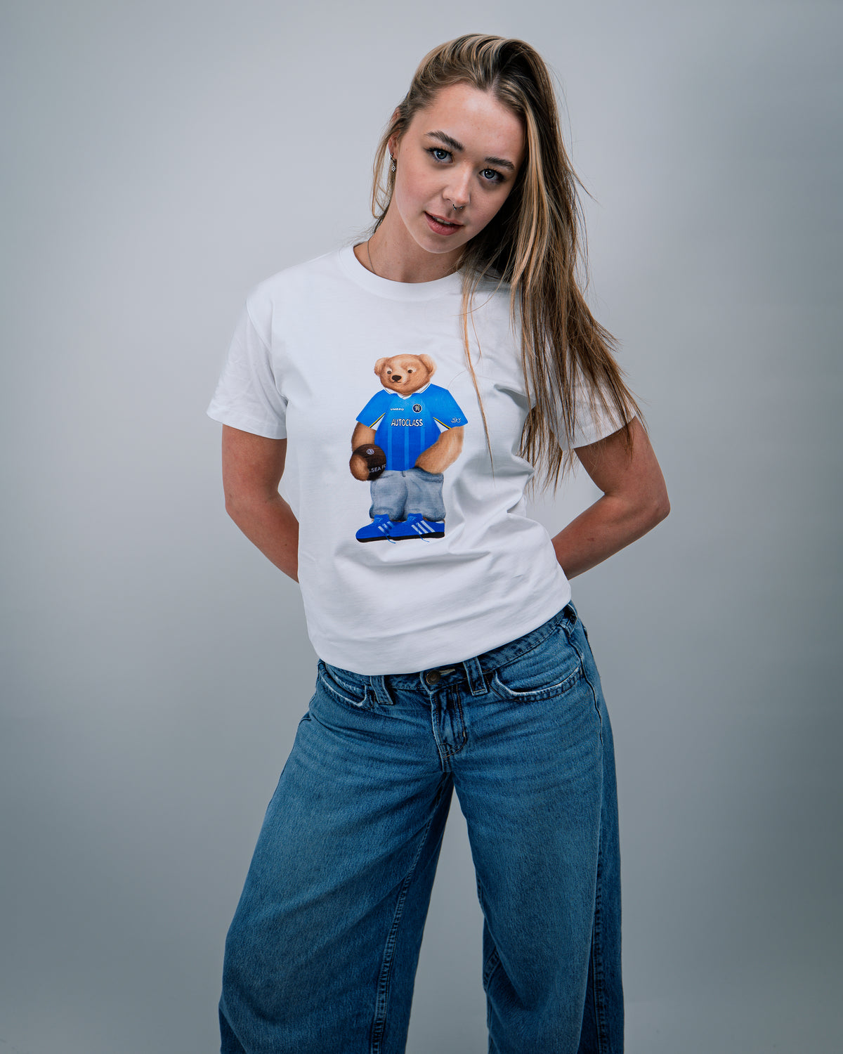 Person wearing a white t-shirt with a graphic of a bear in a blue shirt and shorts on a gray background