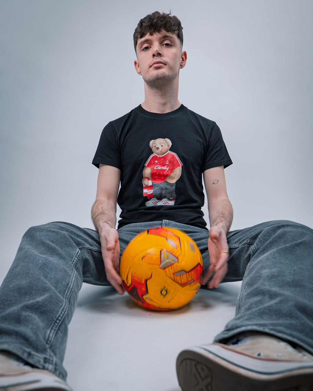 Person wearing a black t-shirt with a graphic design, sitting on the floor with a colorful ball.