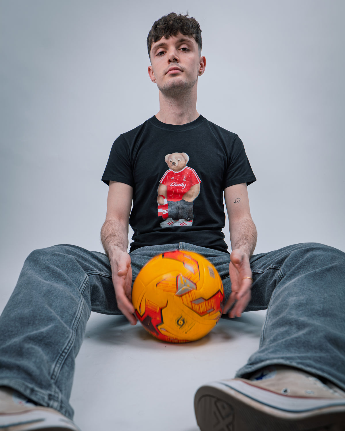 Person wearing a black t-shirt with a graphic design, sitting on the floor with a colorful ball.