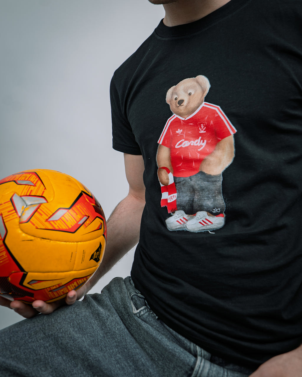 Person wearing a black t-shirt with a teddy bear graphic holding a soccer ball.