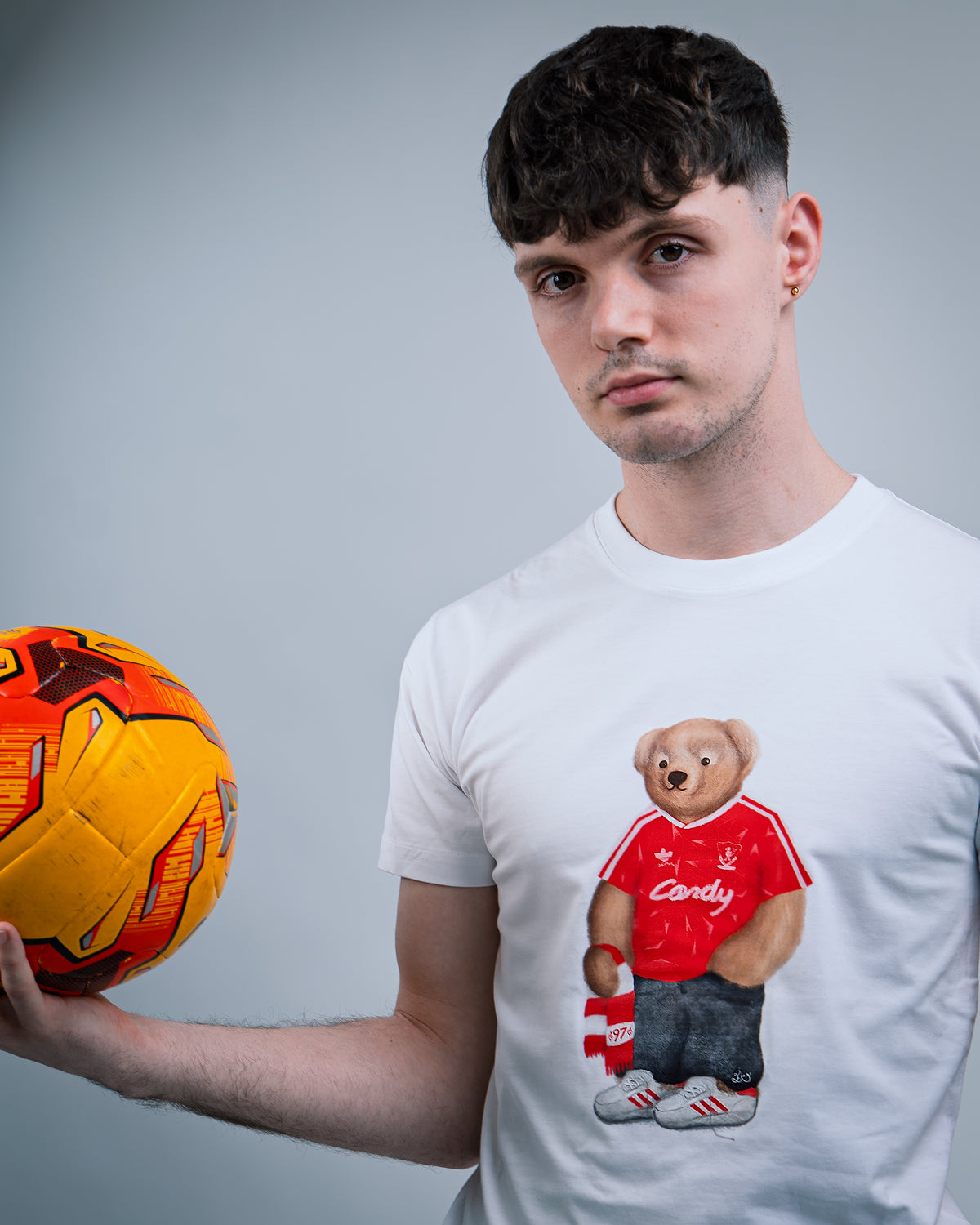 Man holding a soccer ball wearing a white t-shirt with a bear graphic.