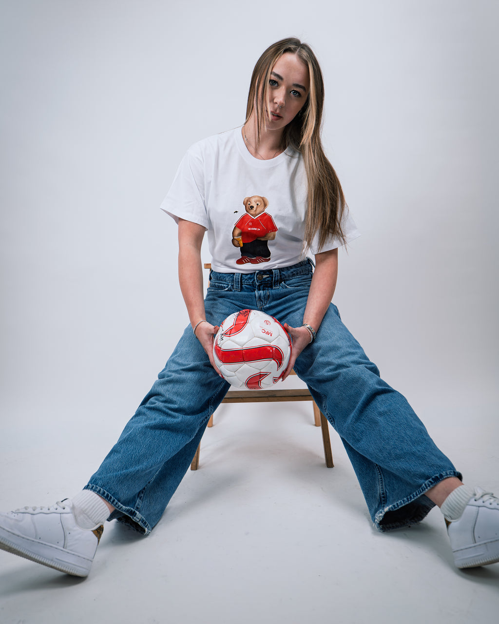Person sitting on a chair holding a soccer ball against a plain background
