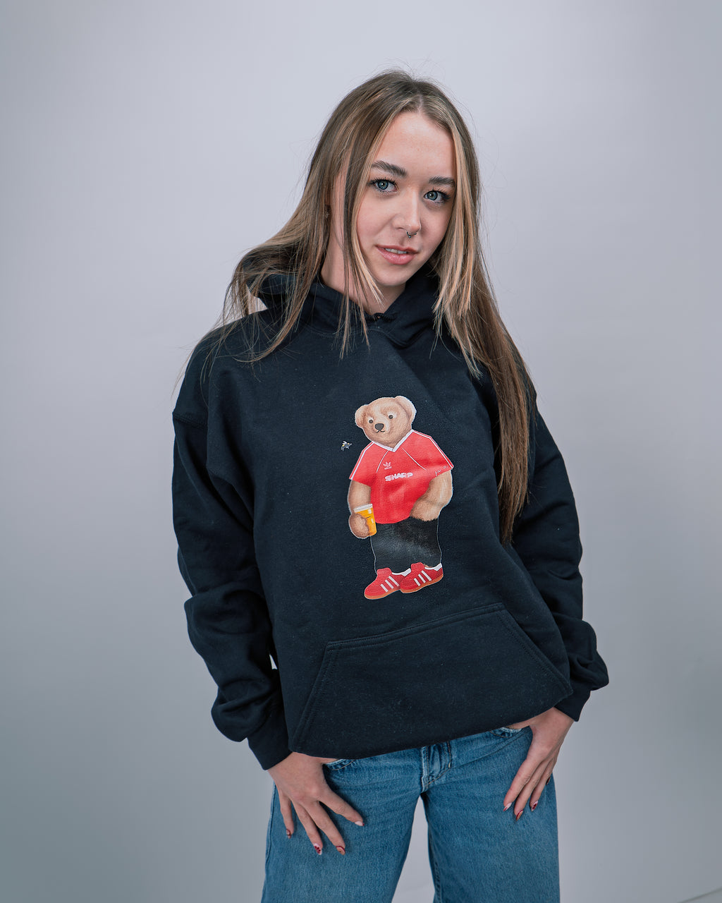 Person wearing a black hoodie with a graphic of a bear holding a drink and wearing sunglasses on a plain background