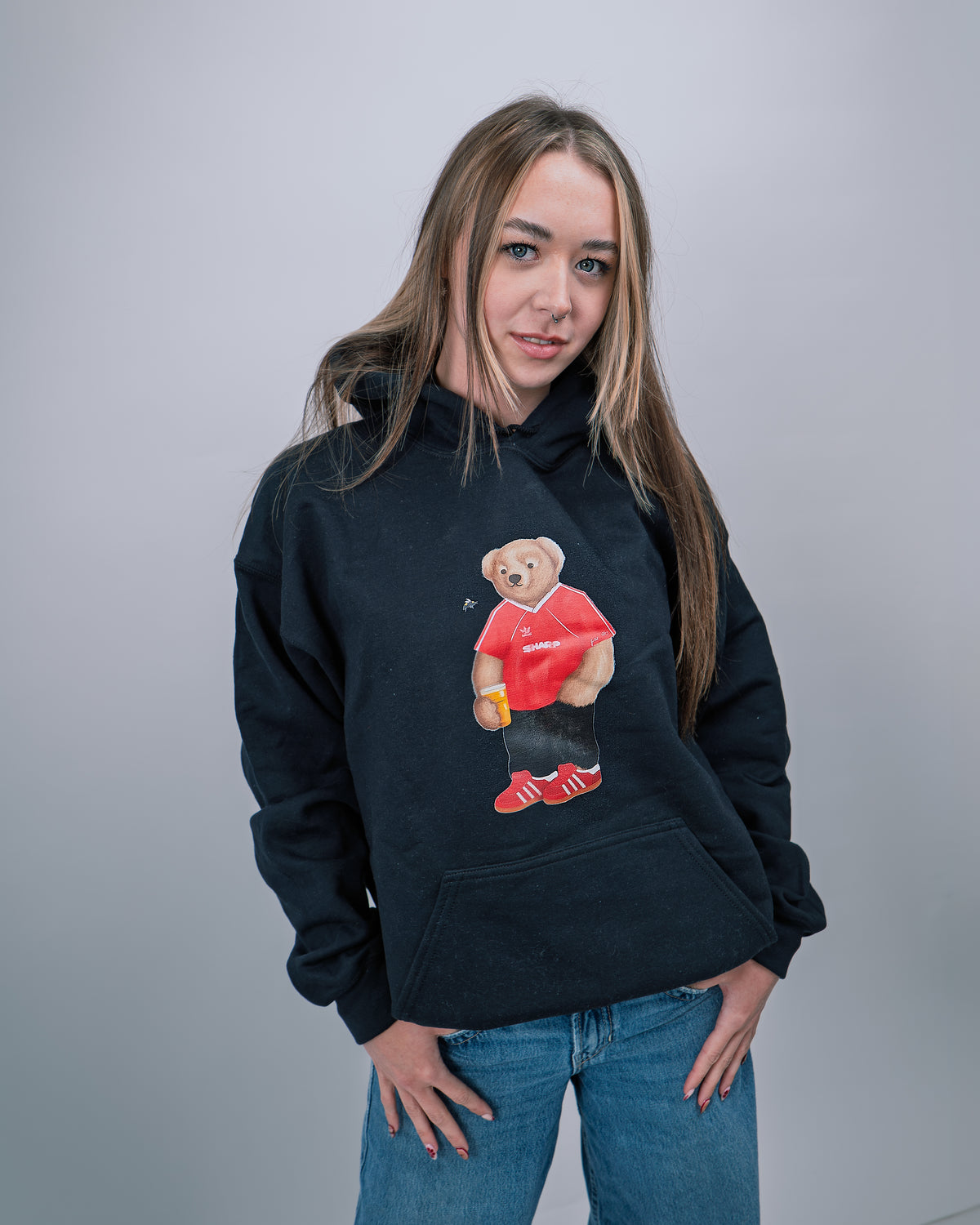 Person wearing a black hoodie with a graphic of a bear holding a drink and wearing sunglasses on a plain background
