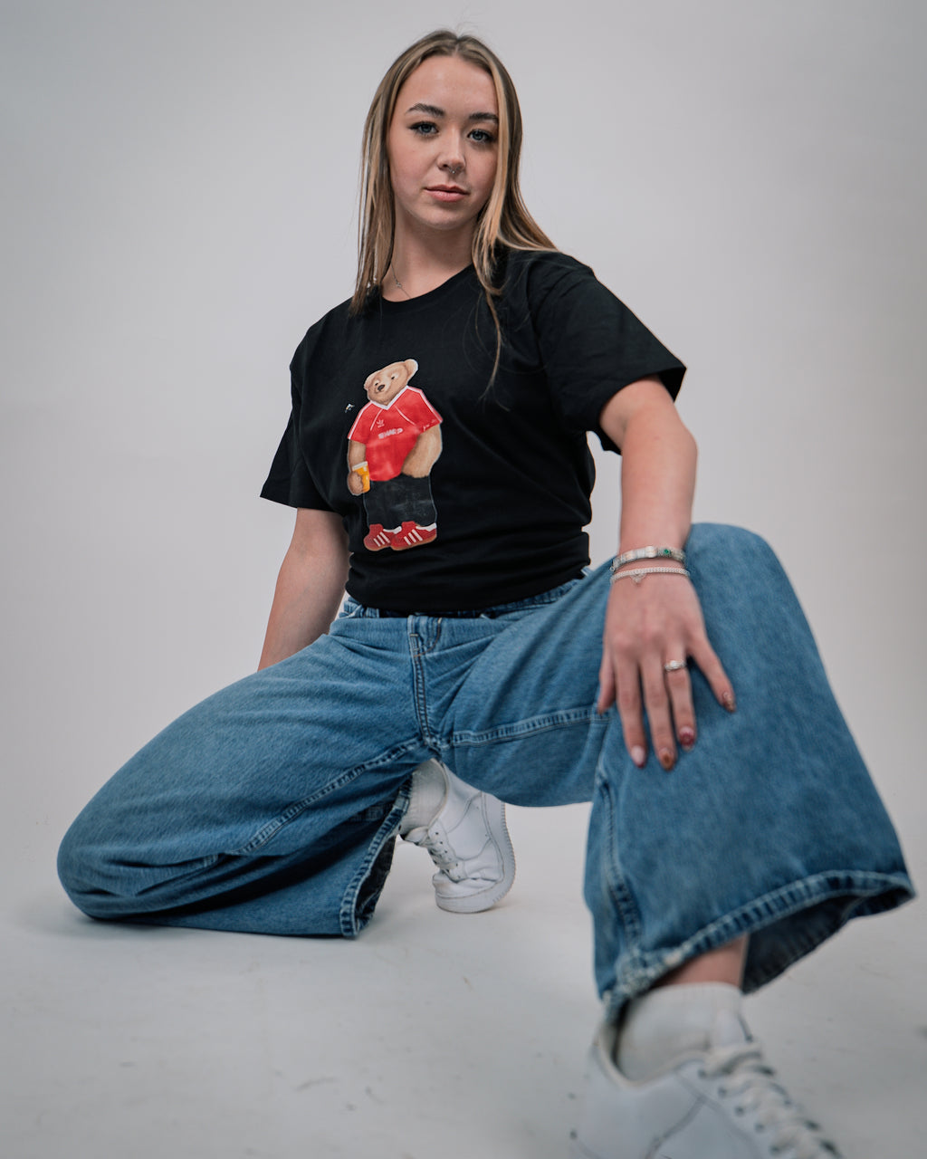 Person wearing a black t-shirt with a graphic design and blue jeans sitting on the floor.
