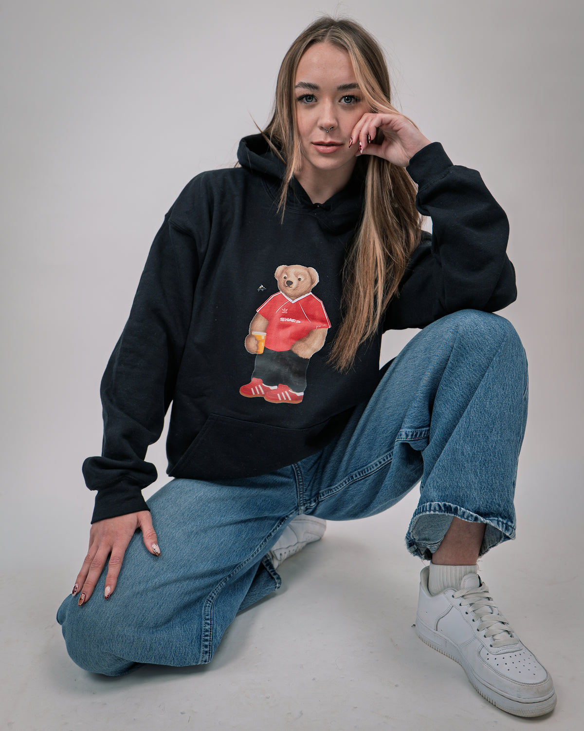Person wearing a black hoodie with a bear graphic, sitting on the floor against a plain background