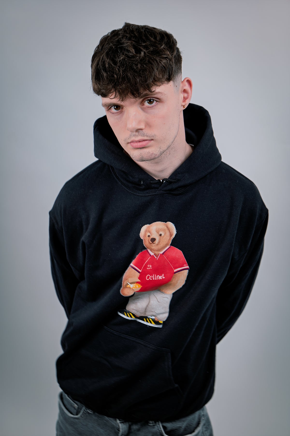 Person wearing a black hoodie with a bear graphic holding a red shirt labeled 'China' on a gray background