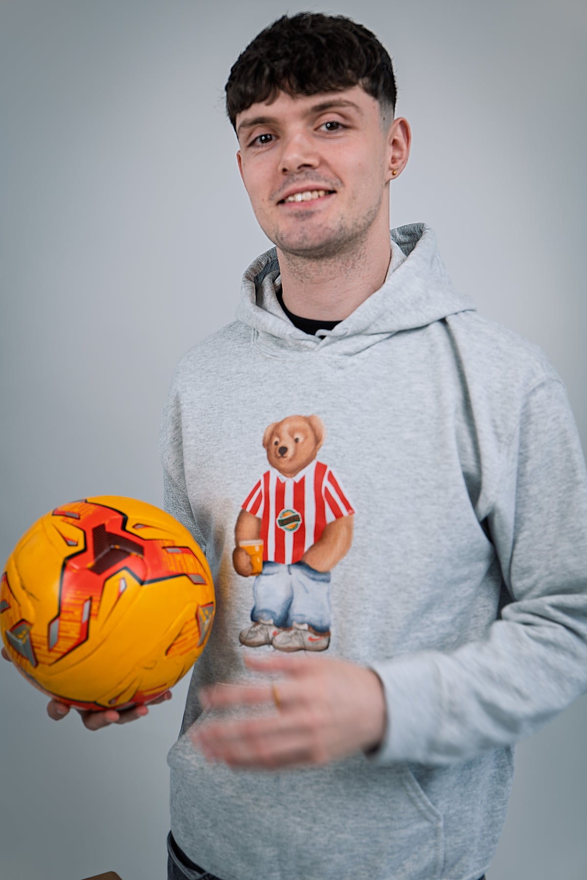 Person wearing a hoodie with a bear graphic holding an orange ball against a gray background