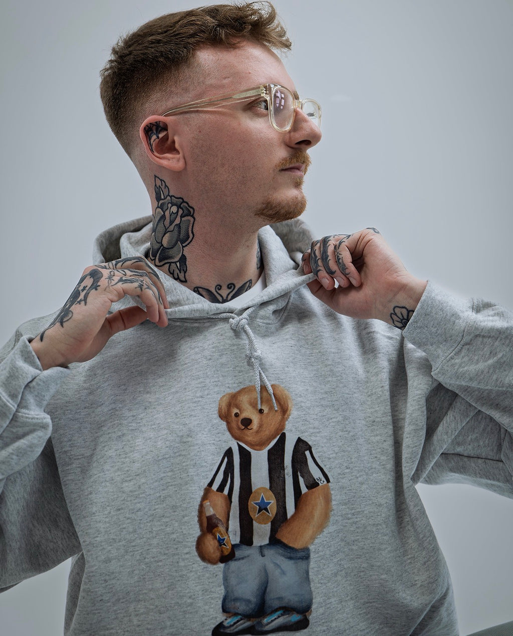 Person wearing a gray hoodie with a bear graphic design on a plain background
