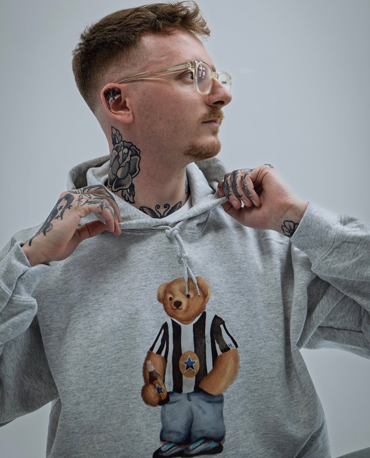 Person wearing a gray hoodie with a bear graphic design on a plain background