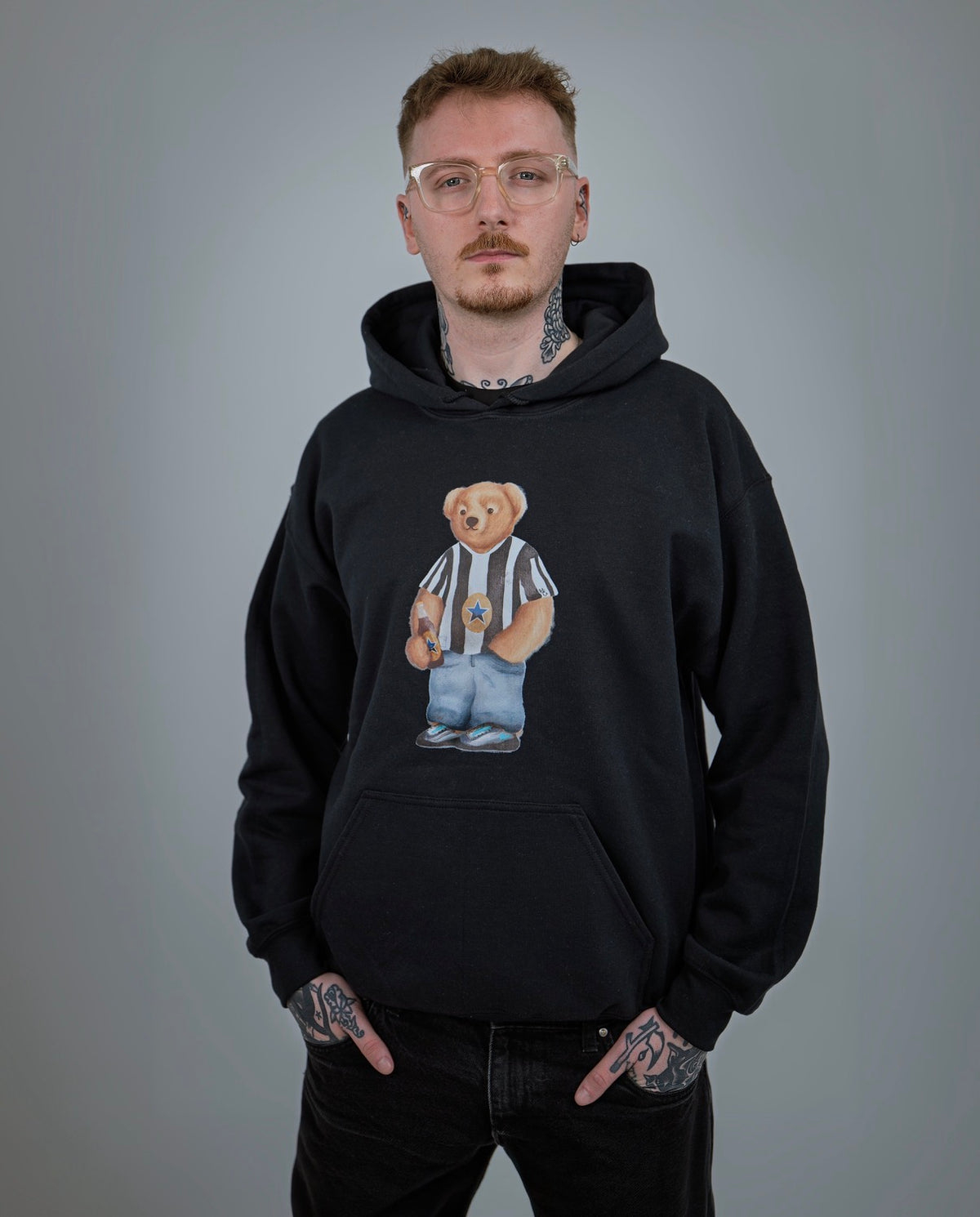 Person wearing a black hoodie with a graphic design of a bear in a referee outfit on a gray background