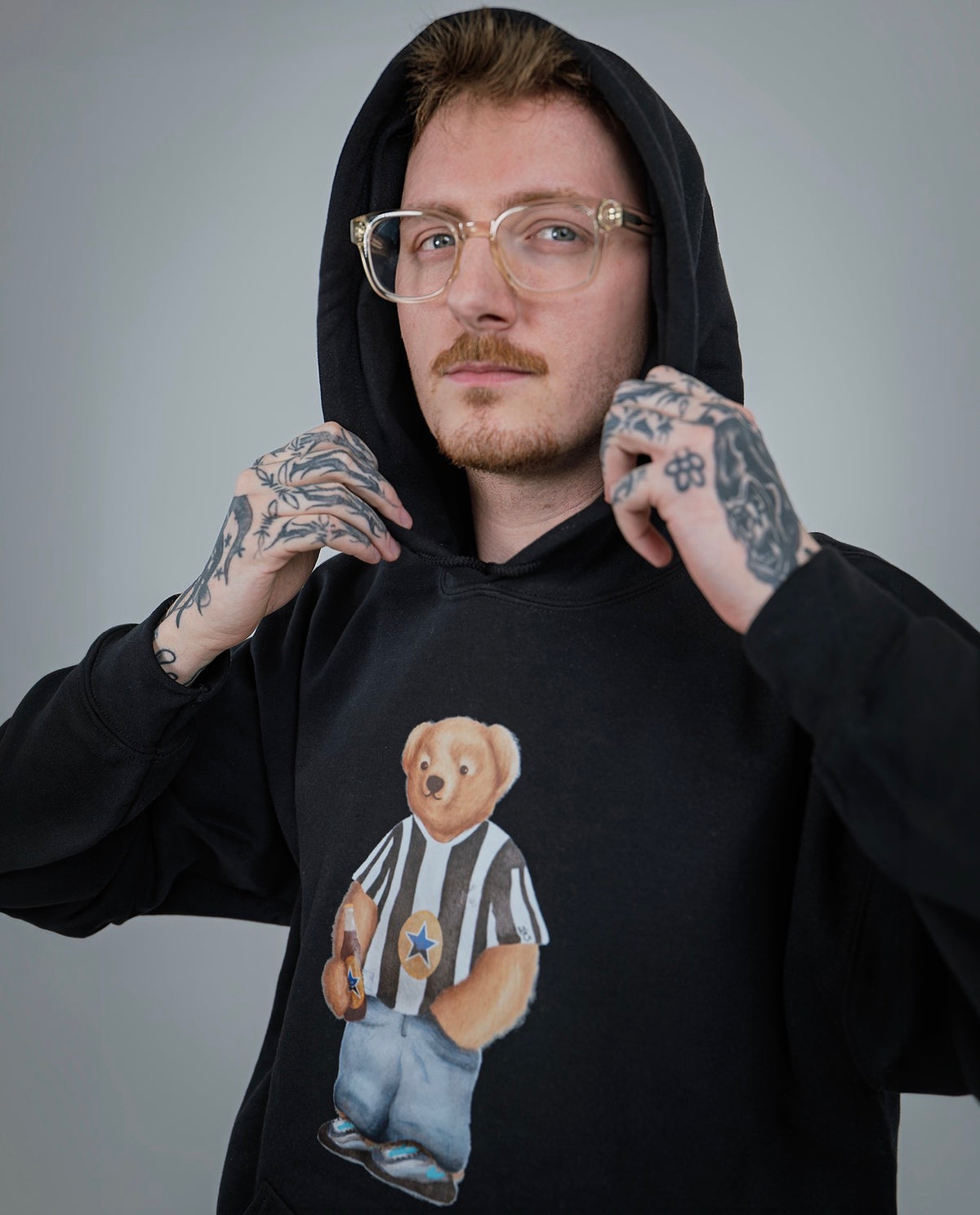 Person wearing a black hoodie with a bear graphic, standing against a plain background