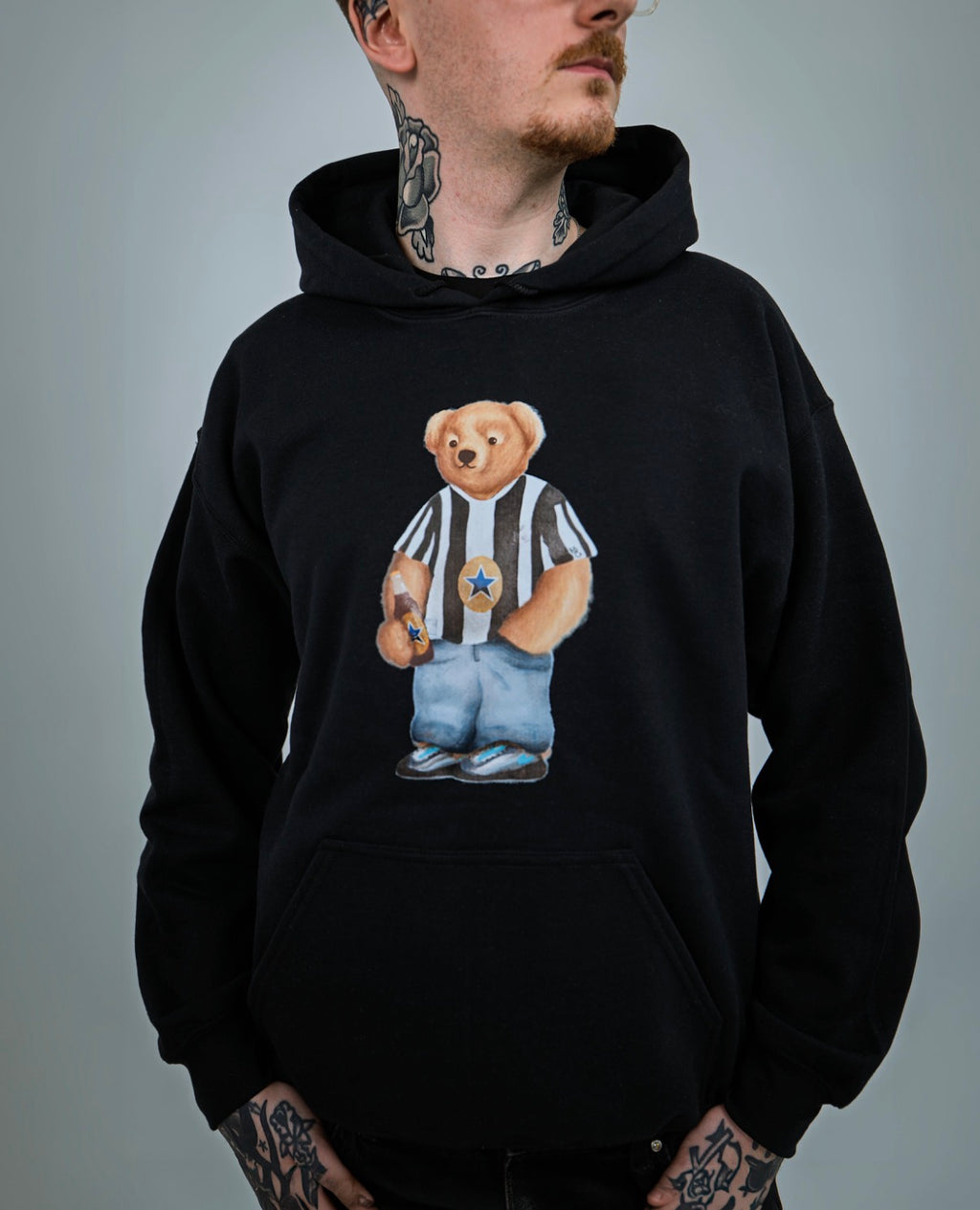 Person wearing a black hoodie with a teddy bear graphic on a gray background