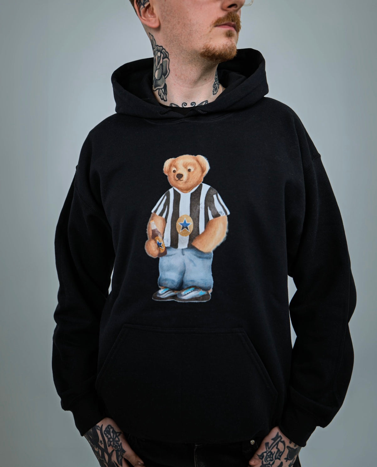 Person wearing a black hoodie with a teddy bear graphic on a gray background