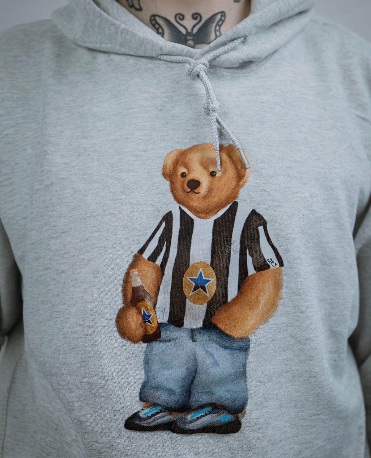 Gray hoodie with a teddy bear design wearing a striped shirt and blue pants.