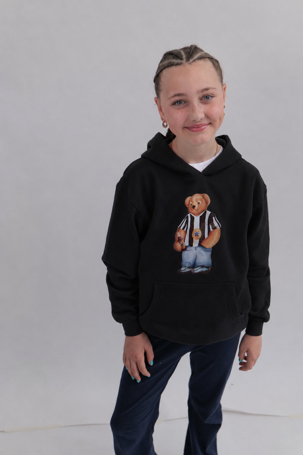 Child wearing a black hoodie with a teddy bear graphic on a plain background