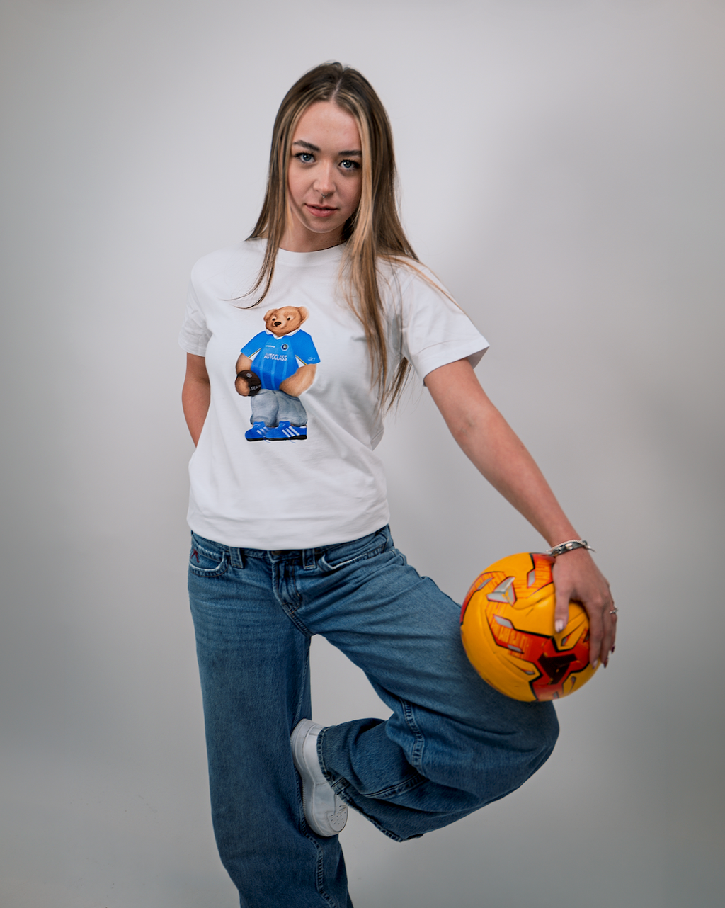Person wearing a white t-shirt with a graphic design, holding a pumpkin, on a plain background