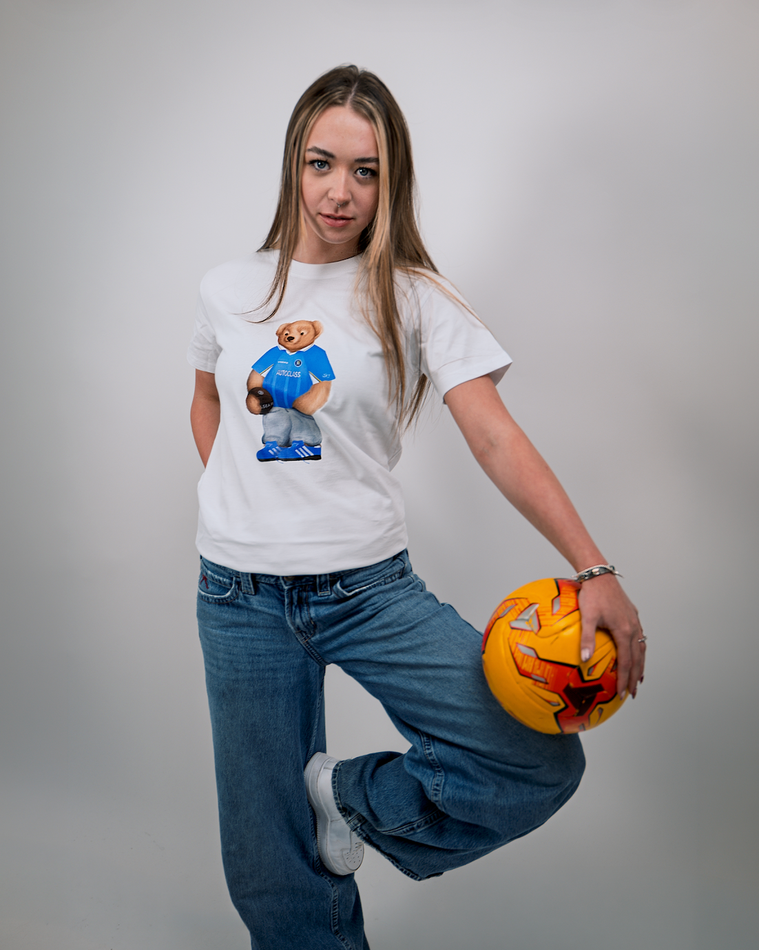 Person wearing a white t-shirt with a graphic design, holding a pumpkin, on a plain background