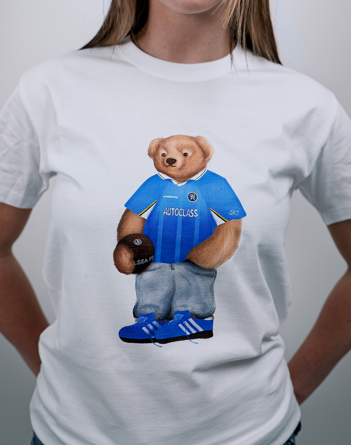 White t-shirt with a bear wearing a blue jersey and shoes, on a plain background.