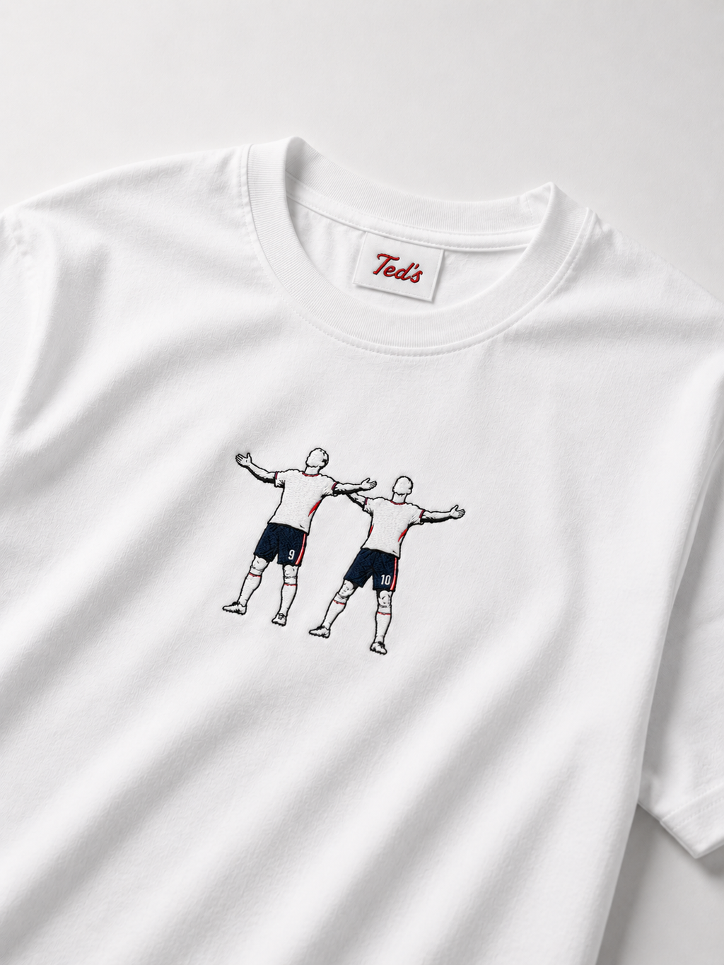 A white short-sleeve crewneck t-shirt featuring embroidered design of two football players Jude Bellingham and Harry kane celebrating. 