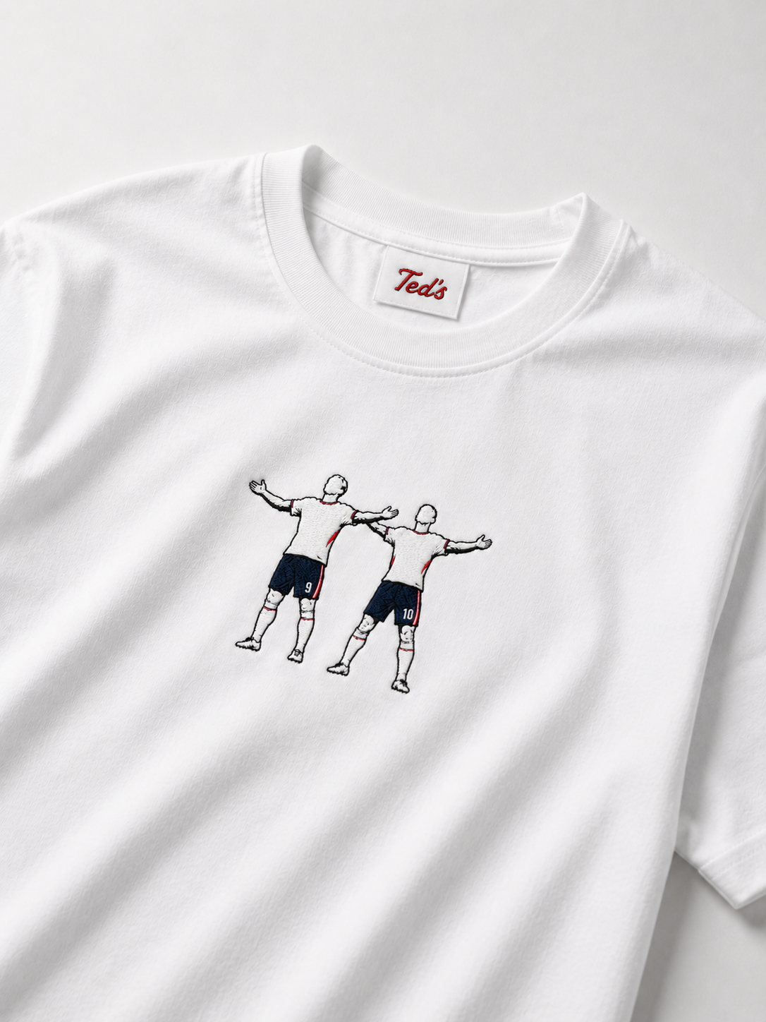 A white short-sleeve crewneck t-shirt featuring embroidered design of two football players Jude Bellingham and Harry kane celebrating. 