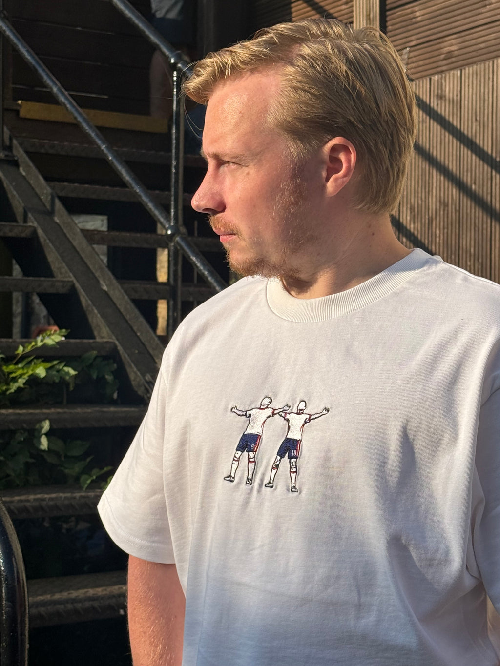 A man wearing a white crewneck t-shirt with a graphic of football players, deck.