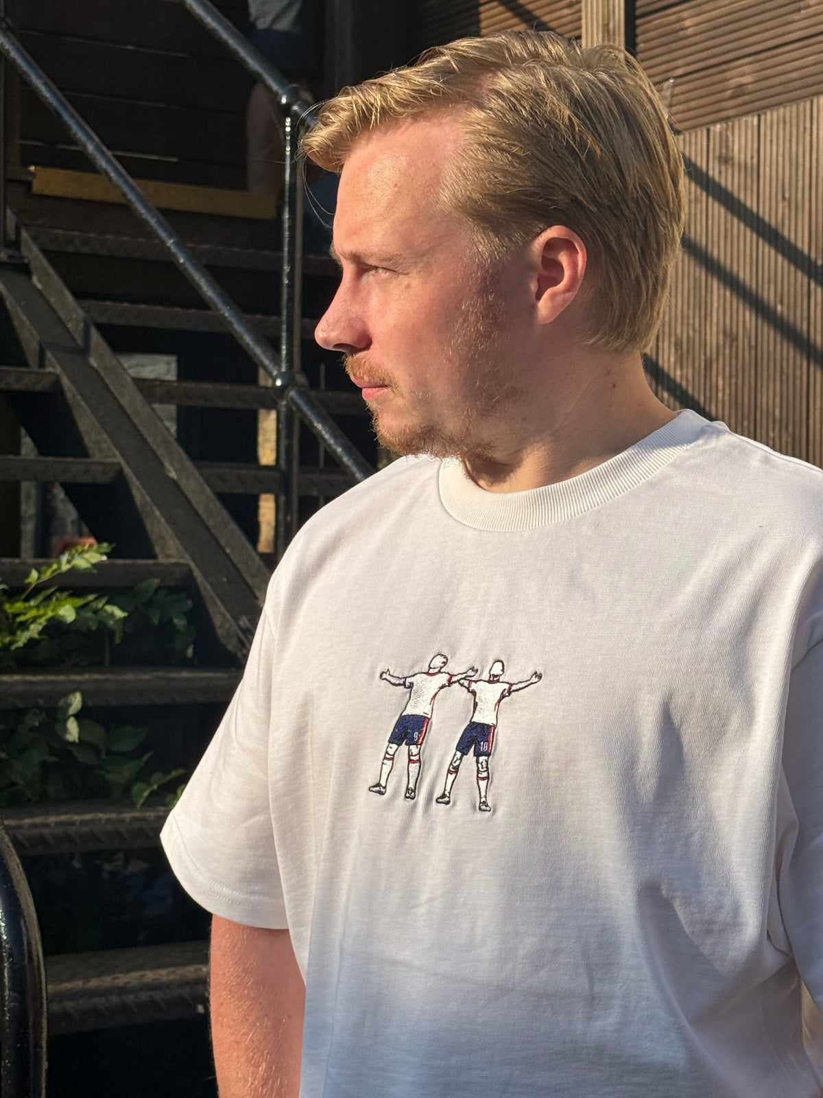 A man wearing a white crewneck t-shirt with a graphic of football players, deck.