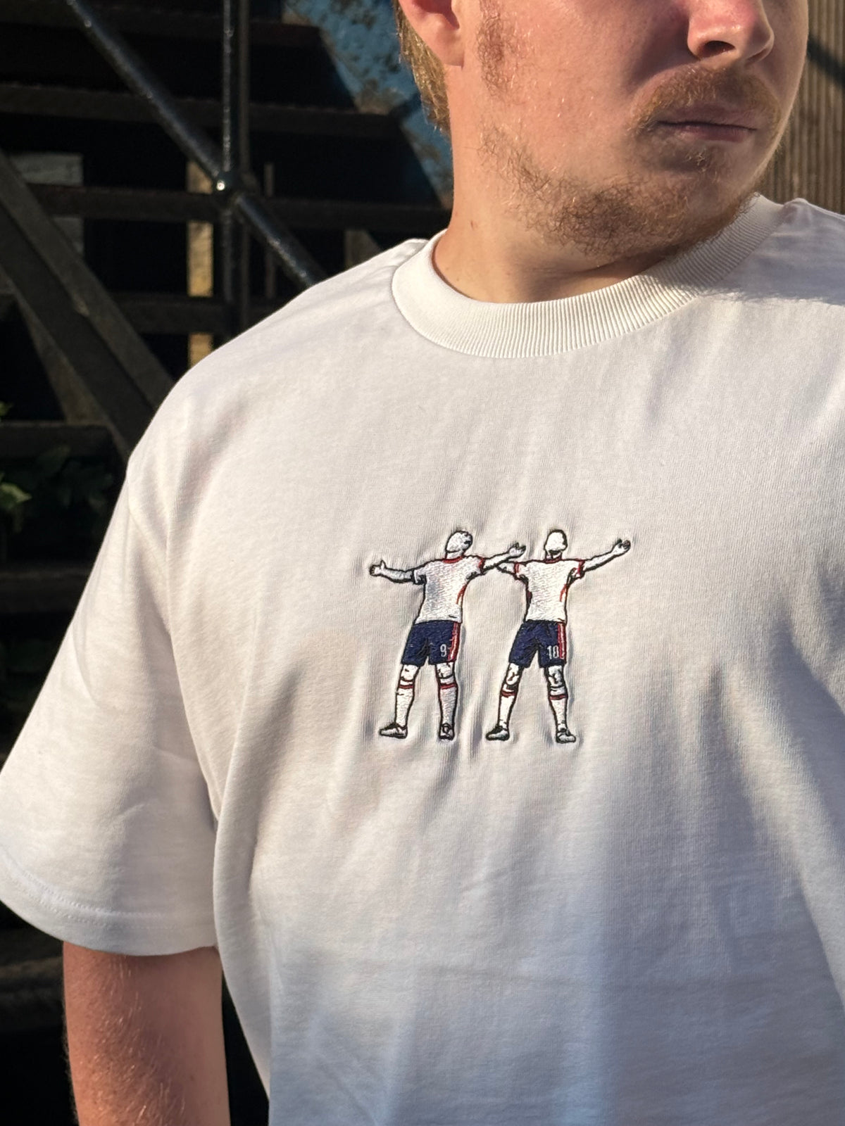 A close-up of a person wearing a white crewneck t-shirt with a graphic print of two soccer players on the chest.