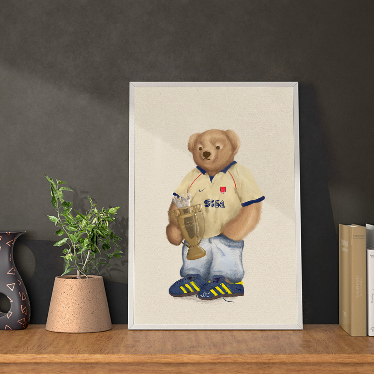 Framed artwork of a teddy bear in sports attire on a shelf with books and a plant.