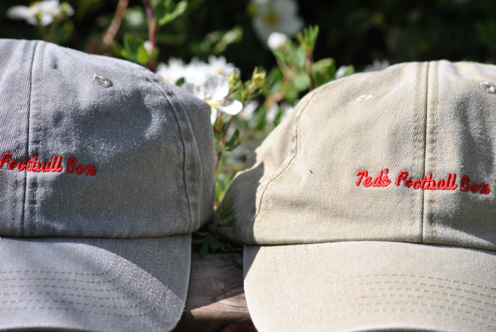 Two baseball caps with 'Ted's Football Club' text on a blurred natural background