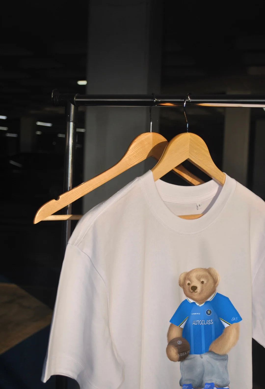 White t-shirt with a bear graphic in a blue shirt on a hanger against a dark background