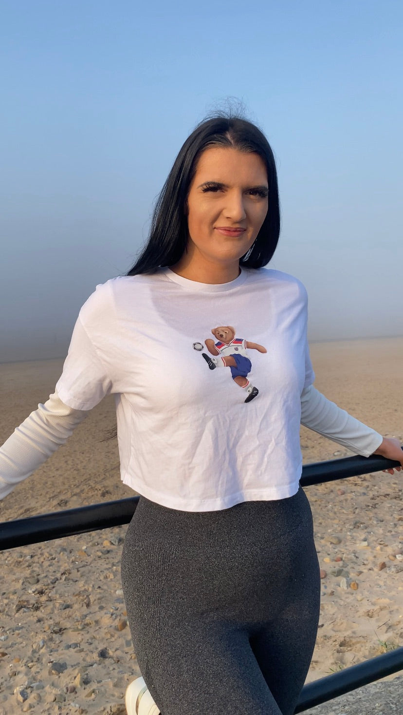 Woman wearing a white long-sleeve shirt with a graphic design, standing on a beach.