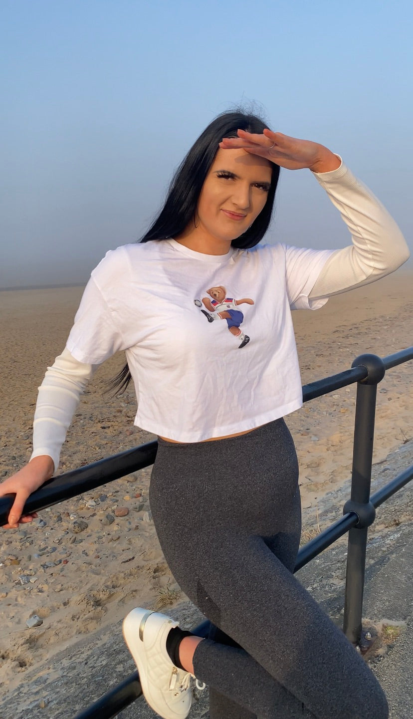 Woman in white long-sleeve shirt with graphic design and gray leggings standing on a beach.